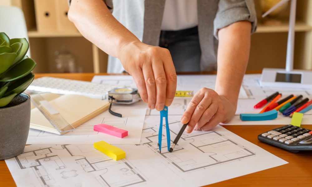 Architect working on a sustainable building project, drawing blueprints with a compass and pencil, surrounded by tools and a miniature wind turbine model