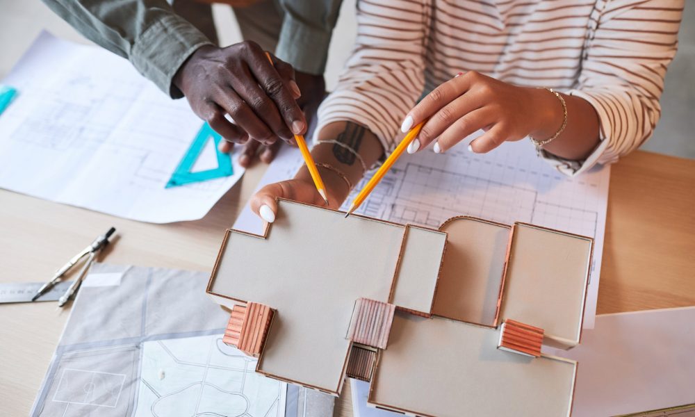 High angle view of architects drawing model of building in team sitting at table with blueprint and mockups