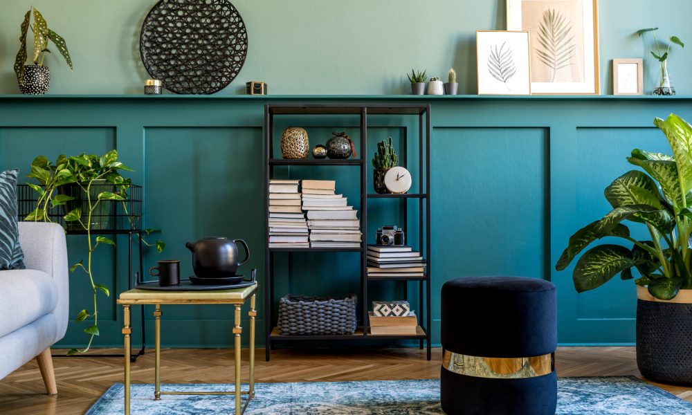 Interior design of living room with gray sofa, design pouf, coffee table, shlef, basket, carpet and elegant personal accessories. Green wood panelling. Modern home decor.