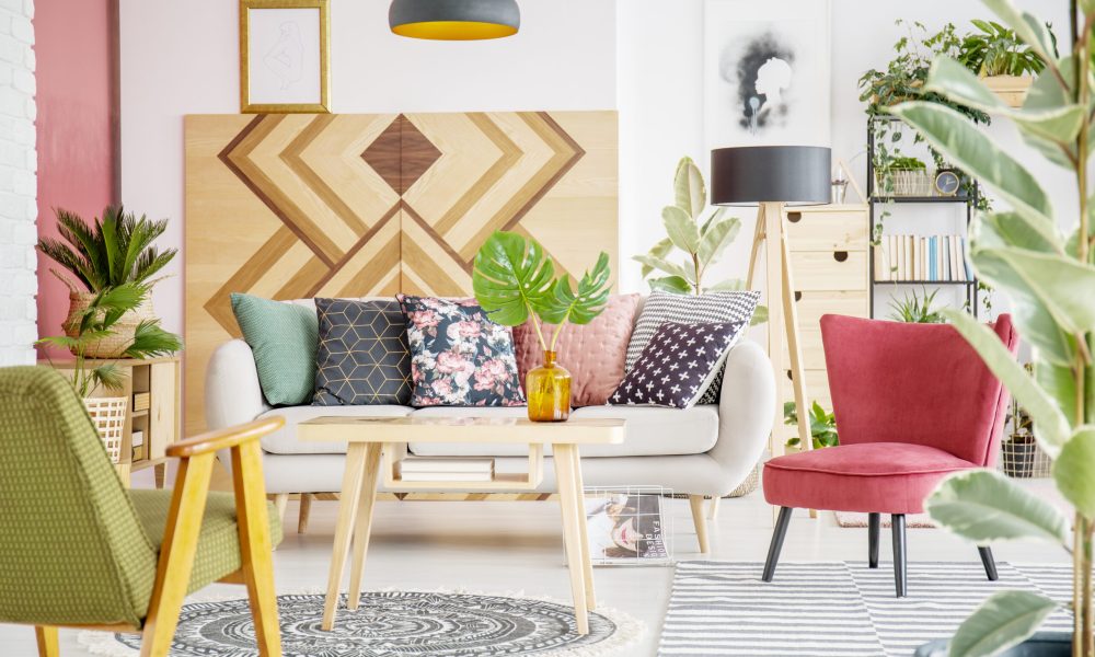 Patterned pillows on sofa next to red armchair in cozy living room interior with wooden furniture