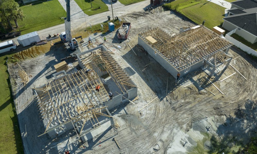 Professional builders and crane truck working on roof construction of unfinished suburban home with wooden frame structure in Florida rural area. Concept of housing development in America.
