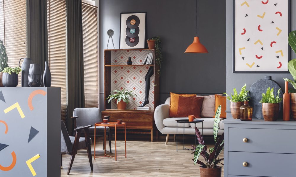 Poster with geometric shapes in spacious grey living room interior with orange table near sofa